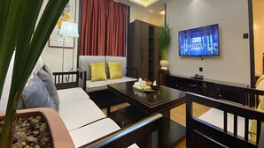 A modern living room with a sofa, a dining table, and a TV mounted on the wall. - Greentree Inn Datong High Speed Railway Station Wa (Datong)