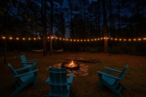 A campfire surrounded by chairs in a forested area with string lights. - Walk to Lake + Stock Tank Pool + Fire Pit (Bastrop)