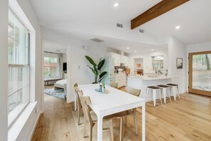 Une cuisine moderne avec des meubles blancs, un îlot central doté de tabourets et une grande fenêtre qui laisse entrer la lumière naturelle.