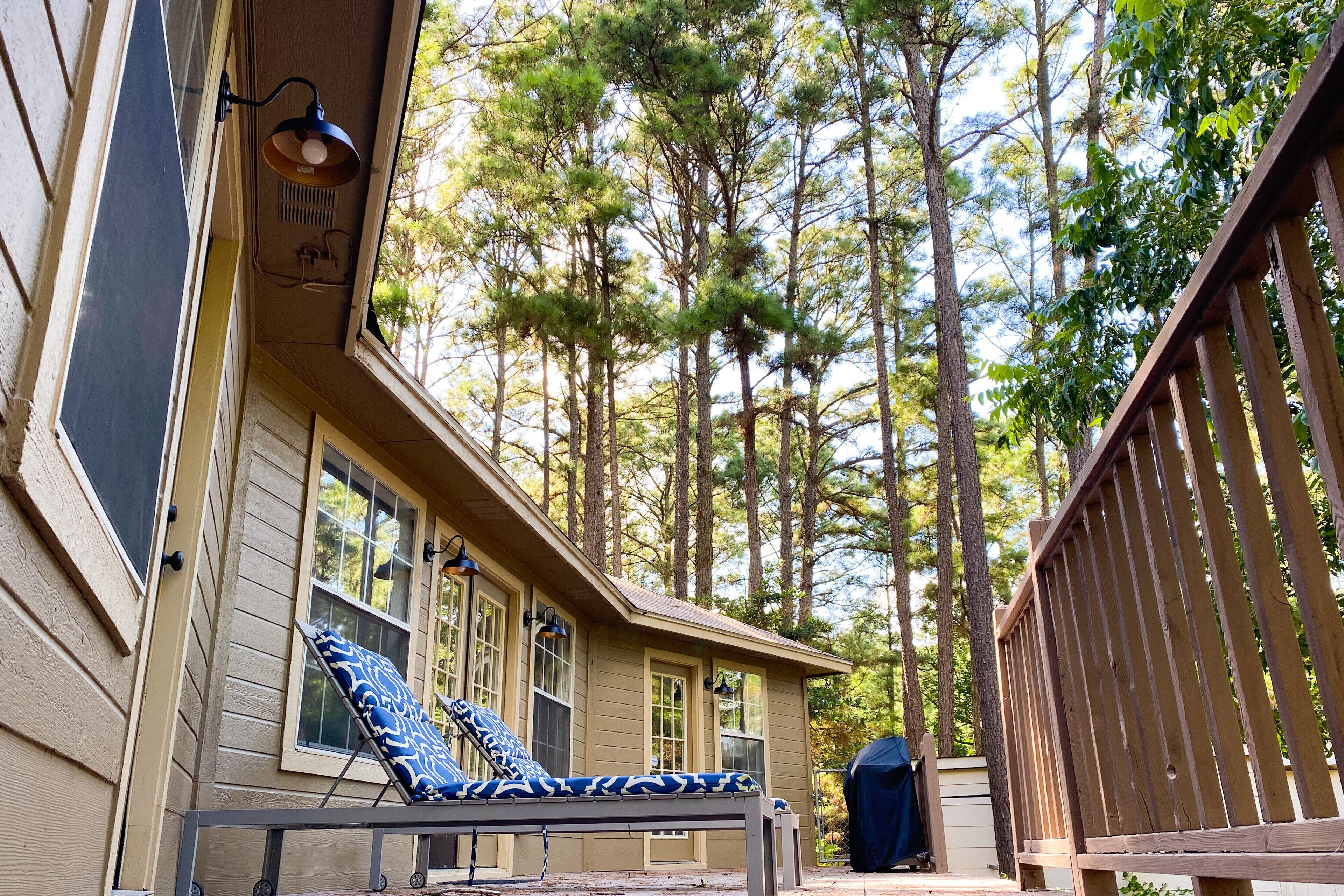 A wooden deck with a lounge chair and a table, surrounded by tall trees.