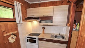 Een compacte keuken met houten kastjes, een fornuis, een spoelbak en een raam met uitzicht op de omgeving.