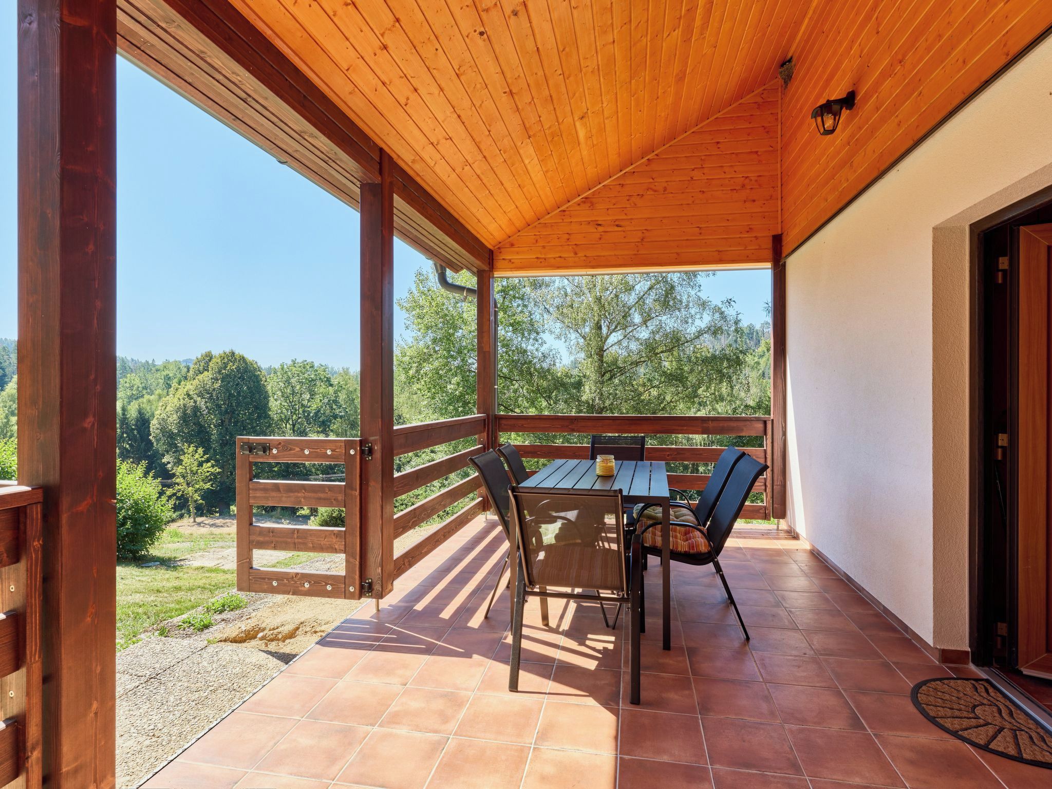 Une terrasse extérieure avec une table et des chaises en bois, une vue sur les arbres et un ciel dégagé.