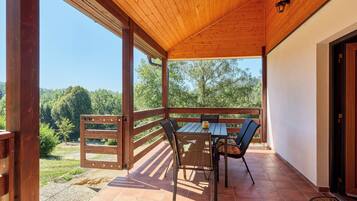 Une terrasse extérieure avec une table et des chaises en bois, une vue sur les arbres et un ciel dégagé.