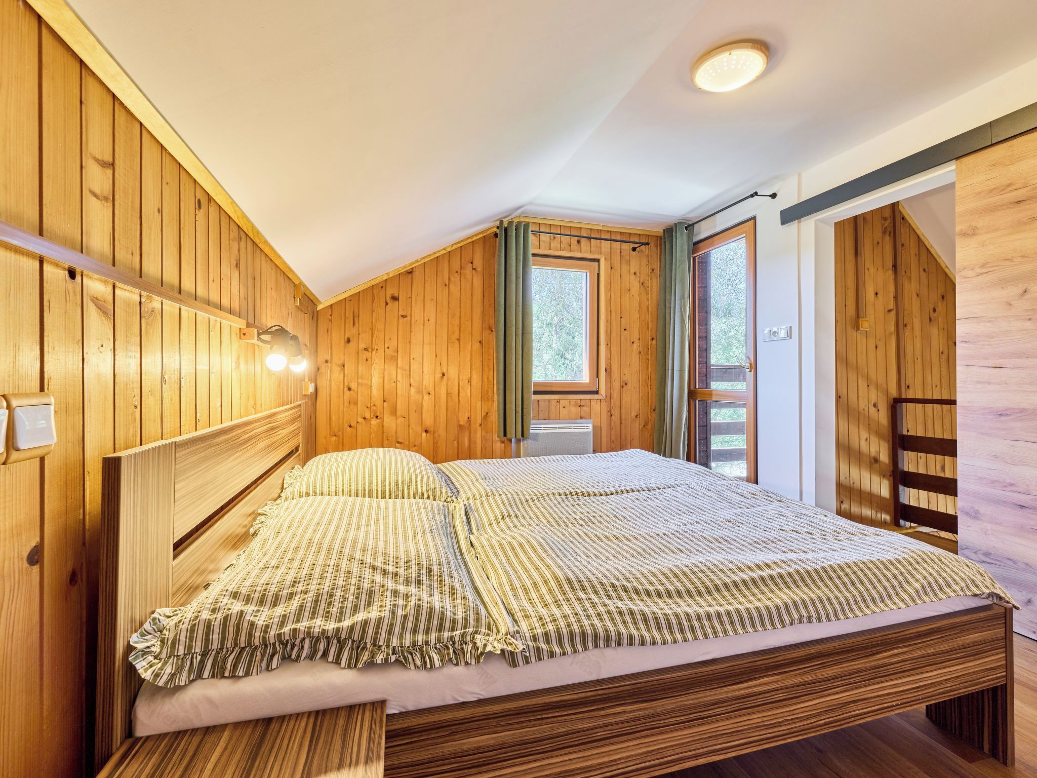 Une chambre aux murs lambrés, avec un lit, une fenêtre et une porte.
