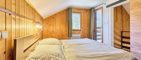 Een slaapkamer met houten lambrisering, een bed, een raam en een deur.