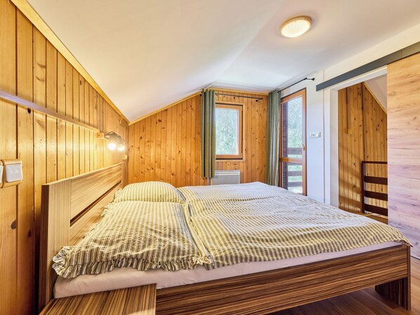 A wooden-paneled bedroom with a bed, a window, and a door.