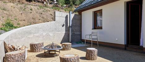 A patio area with a fire pit, seating, and a building with a window and door.