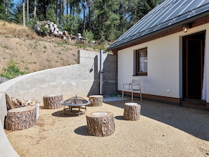A patio area with a fire pit, seating, and a building with a window and door.