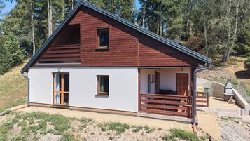 Une cabane à deux étages, dotée d’un toit en pente, d’un porche avec des balustrades en bois et d’une petite fenêtre à l’étage supérieur.
