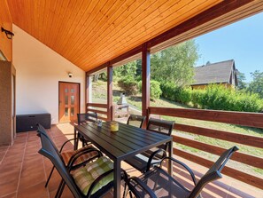 A covered patio with a table and chairs, a door, and a view of a house and trees.