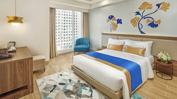 A hotel room with a bed, a desk, a chair, a nightstand, and a window with a view of buildings.
