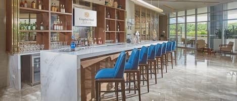 A bar area with a marble counter, blue bar stools, and shelves stocked with bottles and glasses.