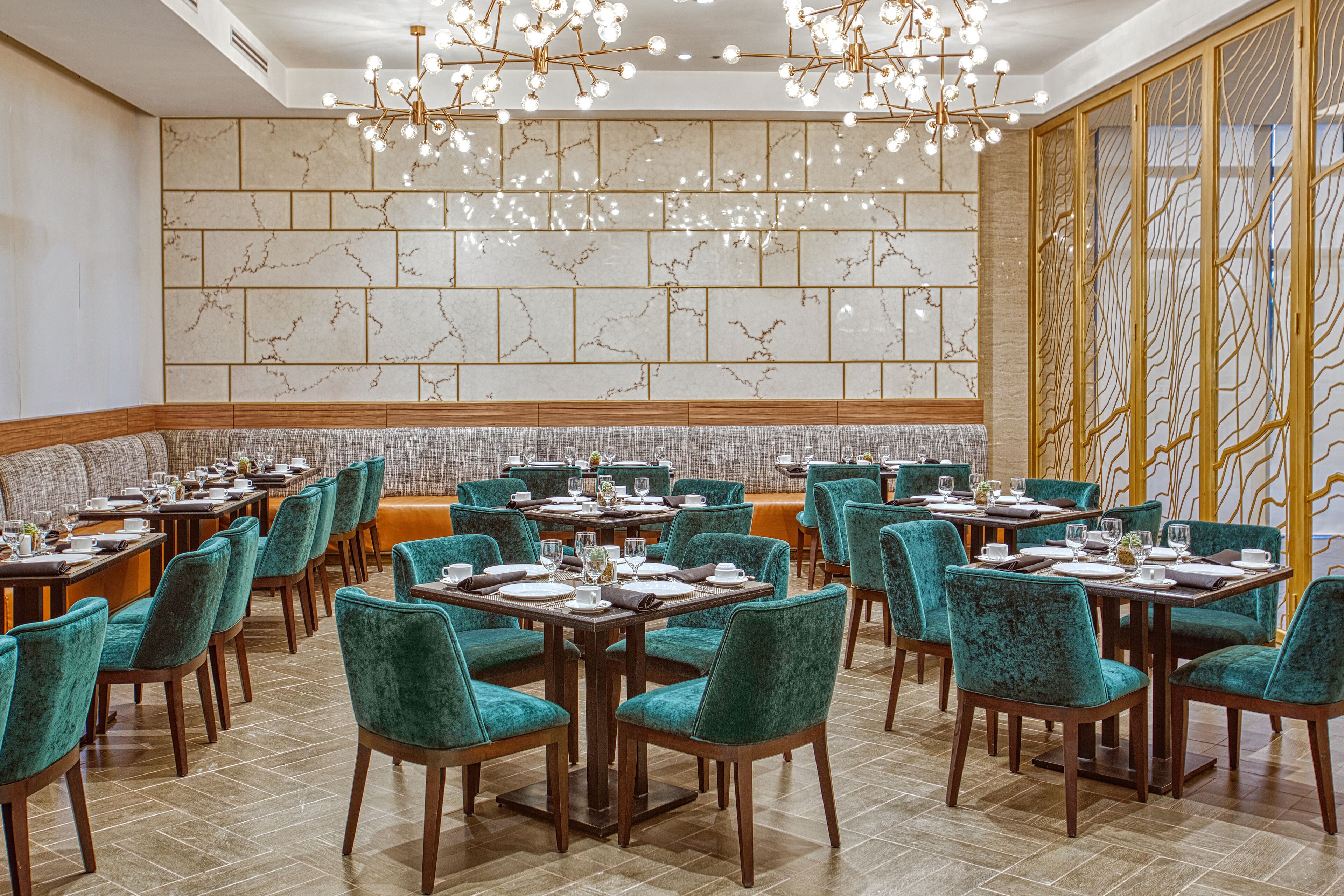 A dining area with teal upholstered chairs, wooden tables, and a decorative wall with a geometric pattern.