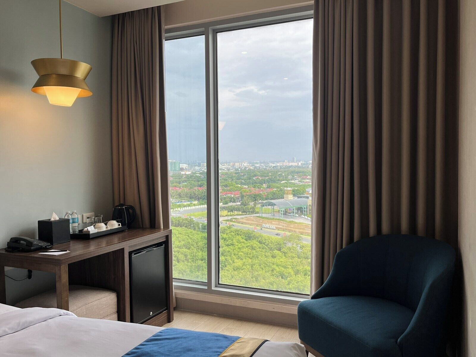 Una habitación de hotel con un ventanal grande, un escritorio con lámpara, una silla y una cama.