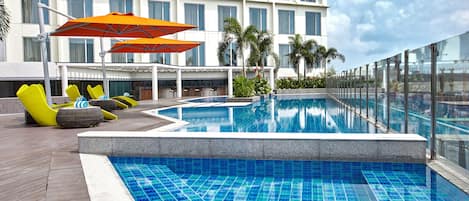 A swimming pool with a tiled deck, lounge chairs, and umbrellas.