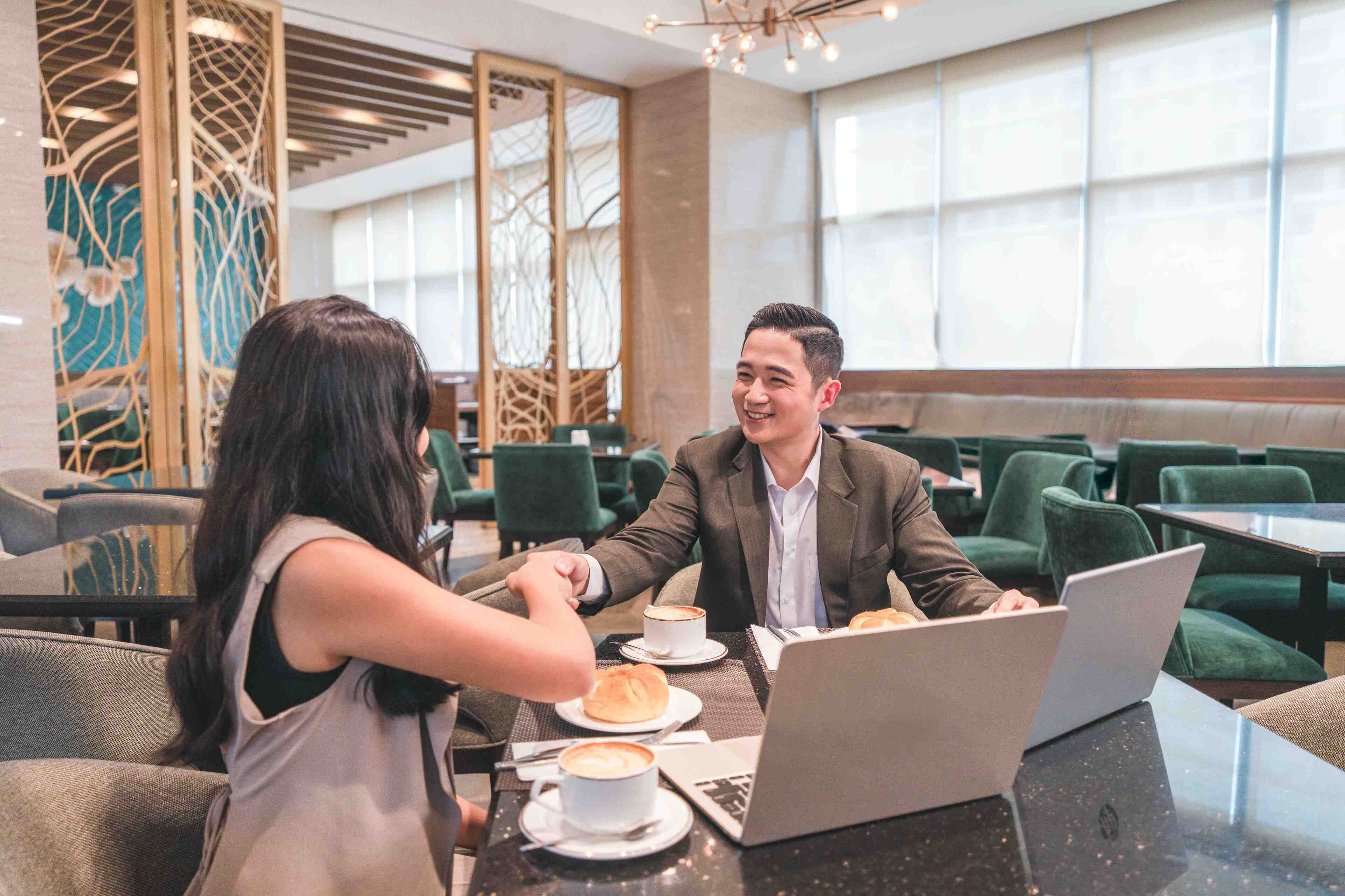 Een modern café met groen gestoffeerde stoelen en tafels, een laptop op een tafel en een koffiekop op een andere.