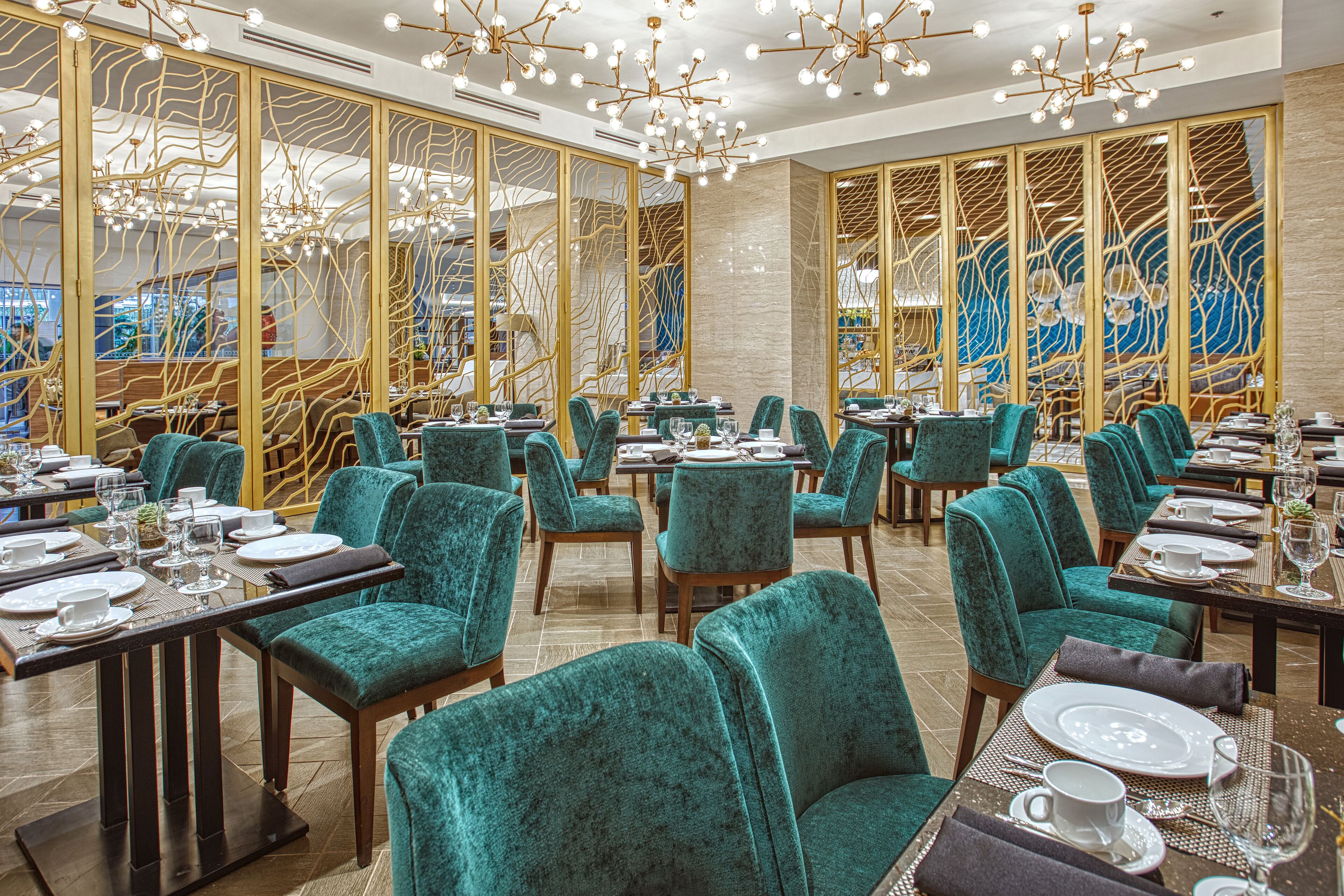 A restaurant with teal upholstered chairs, wooden tables, and a decorative ceiling light fixture.