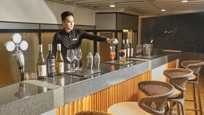 A bar area with a bartender preparing drinks, a counter with bottles and glasses, and wicker chairs. - Kingsford Hotel Manila Bay (Parañaque)