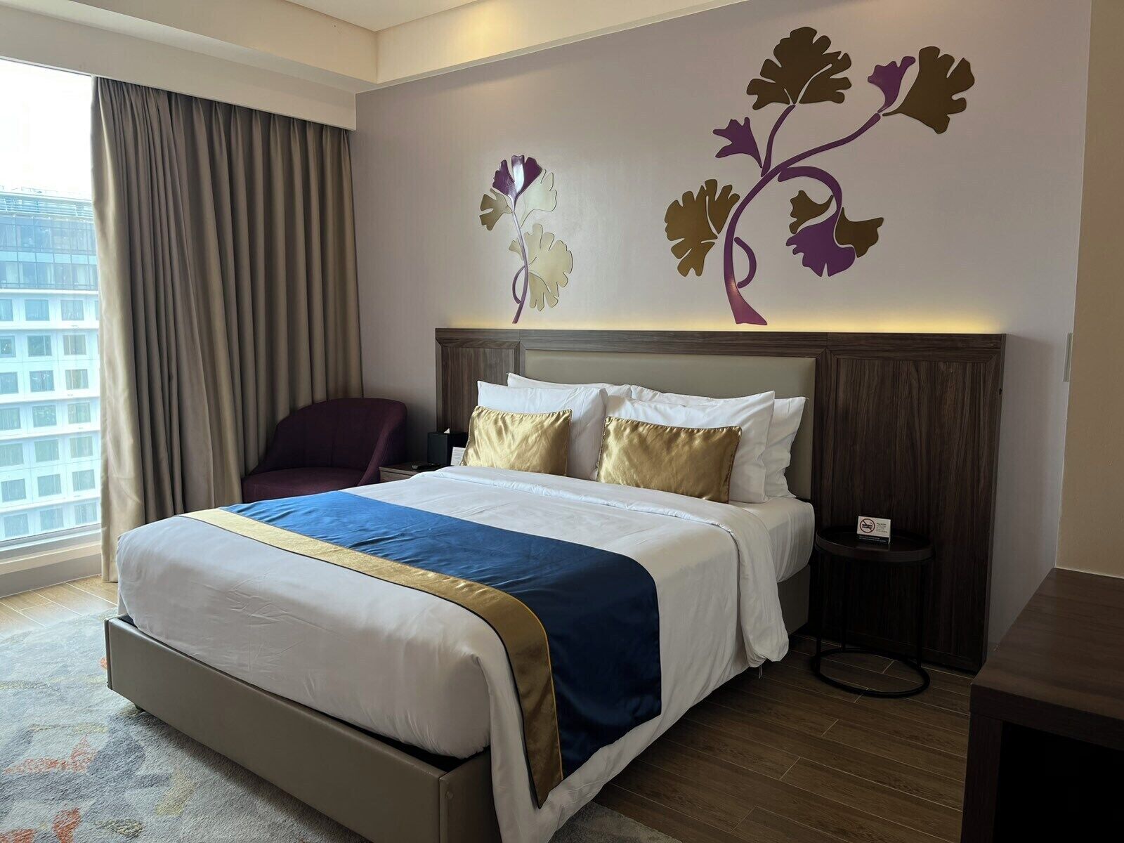 A hotel room with a large bed, a nightstand, a chair, and a wall decoration.