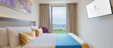 A hotel room with a large bed, a view of the city, and a framed picture on the wall.