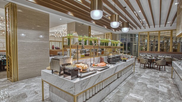 A modern restaurant with marble flooring, a central buffet with various dishes, and a seating area with tables and chairs. - Kingsford Hotel Manila Bay (Parañaque)