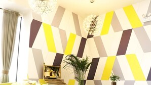Un interior moderno con una pared de diseño geométrico, un sofá, sillas, una mesita y una planta.