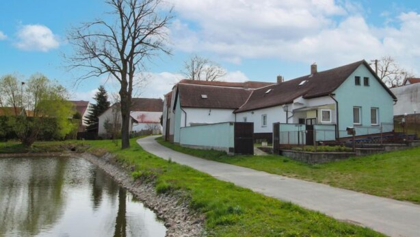Een rij huizen aan een rustig water, met een geplaveid pad dat door het groen loopt.