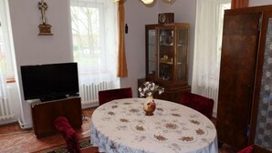 Een eetgedeelte met een ronde tafel, rode bekleden stoelen, een vaas met bloemen, een televisie en een houten kast.