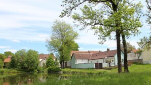Een rustgevende situatie aan een meer, met een klein huis met schuin dak en een omheind erf.