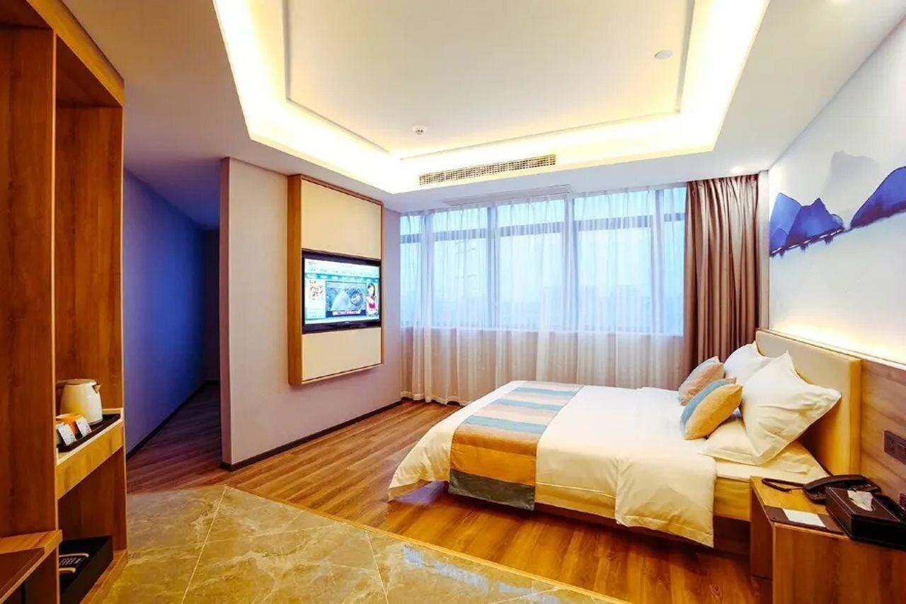 Une chambre d’hôtel avec un lit, une télévision, un bureau et une fenêtre avec des rideaux.