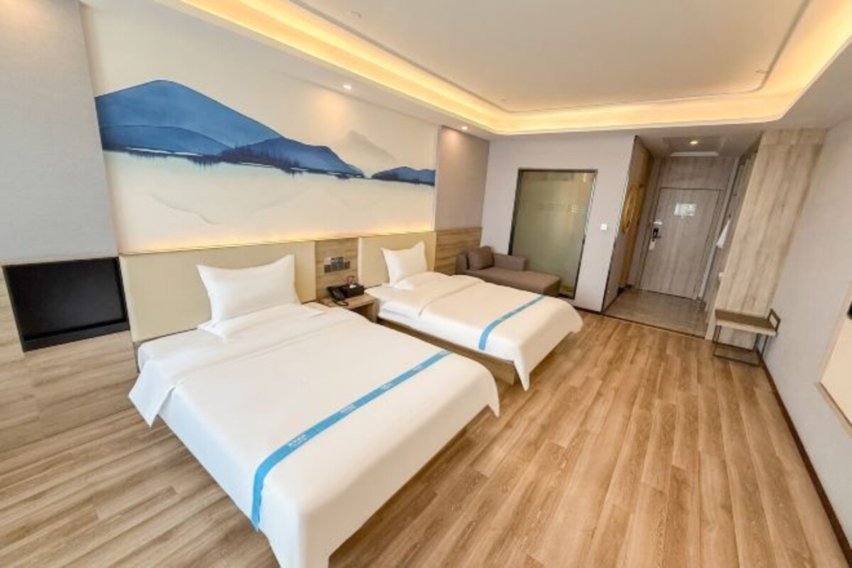 A hotel room with two beds, a large painting on the wall, and a wooden floor.