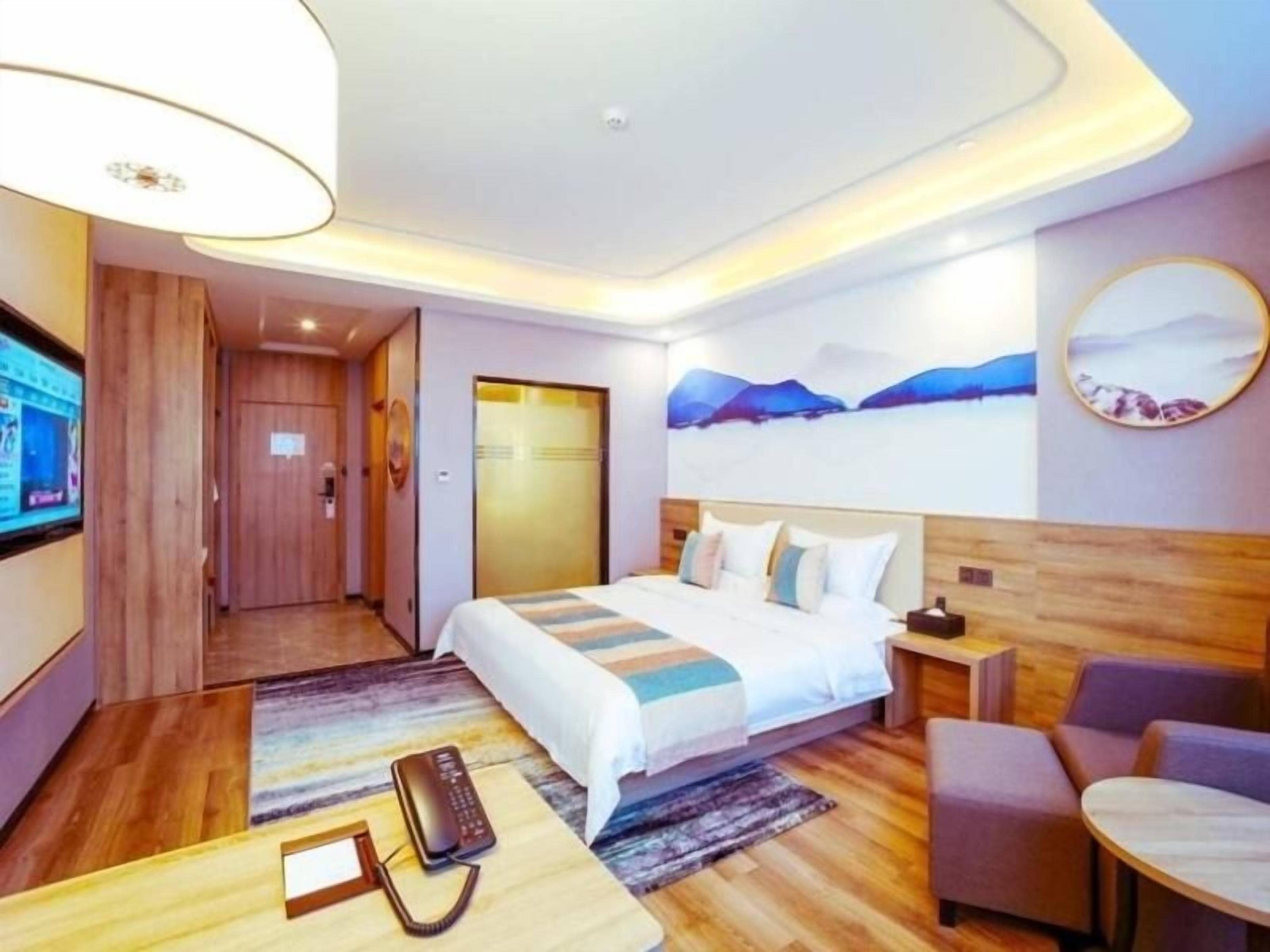 Habitación de hotel moderna con una cama grande, un escritorio, una silla, un televisor y un cuadro en la pared.