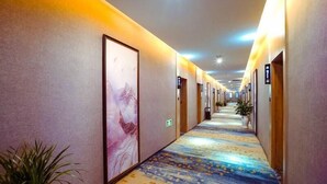 A hotel hallway with a patterned carpet, framed artwork on the walls, and doors with room numbers.