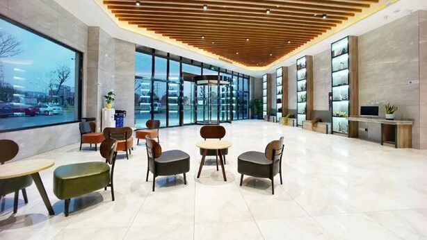 A modern lobby with a wooden ceiling, glass walls, and a seating area with tables and chairs.