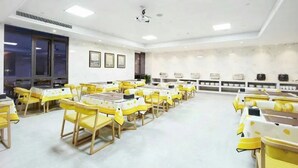 A spacious dining area with yellow chairs and tables, a white ceiling, and a marble wall.