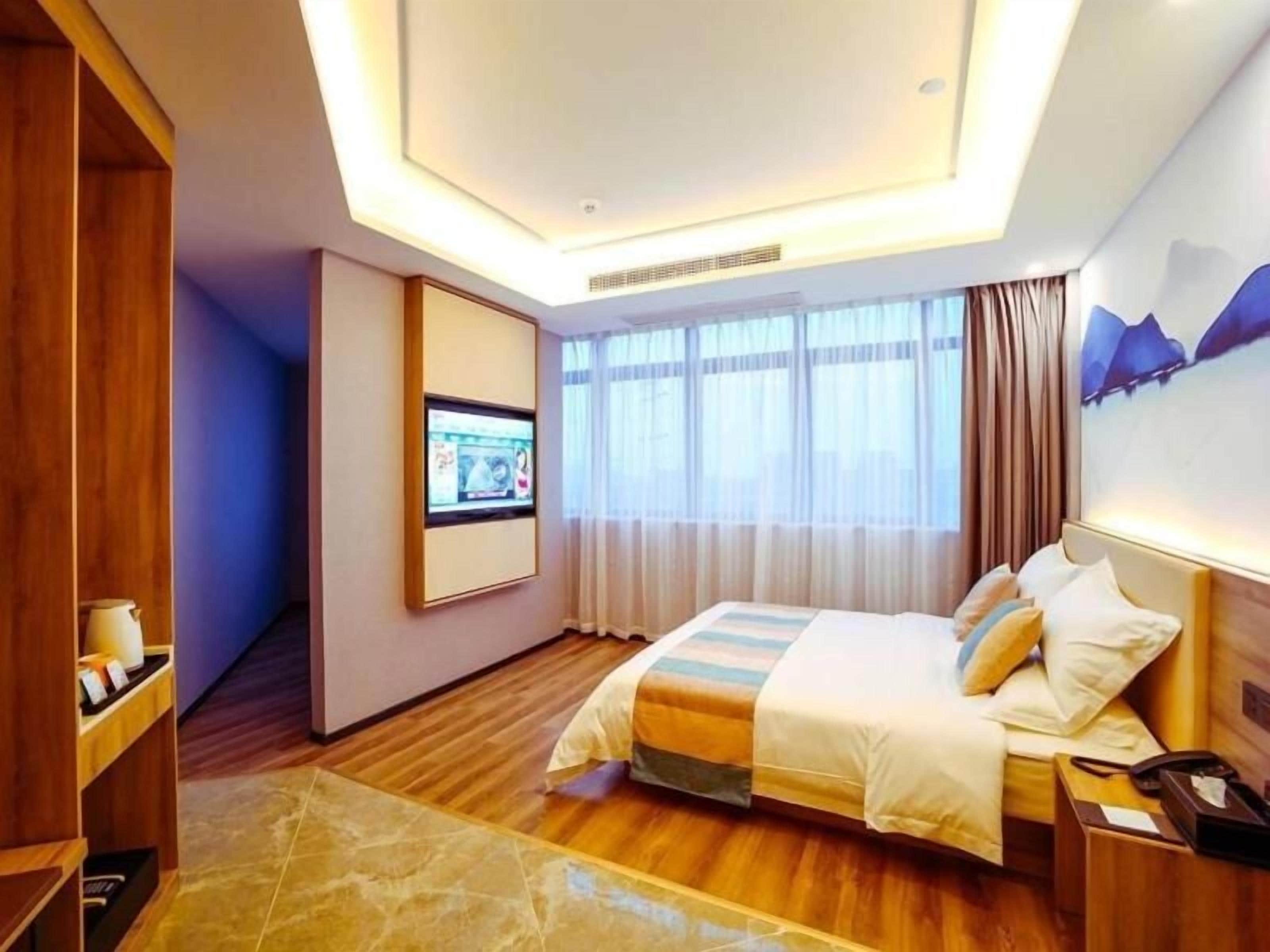 A hotel room with a bed, a television mounted on the wall, and a window with curtains.