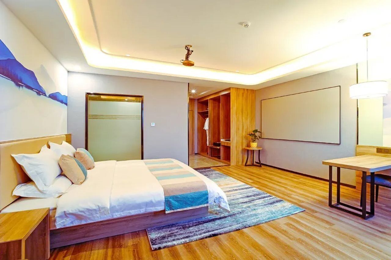 A modern hotel room with a large bed, a wooden floor, a desk, and a wardrobe.