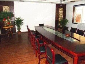 Conference room with a long table and six chairs, surrounded by potted plants and a small side table.
