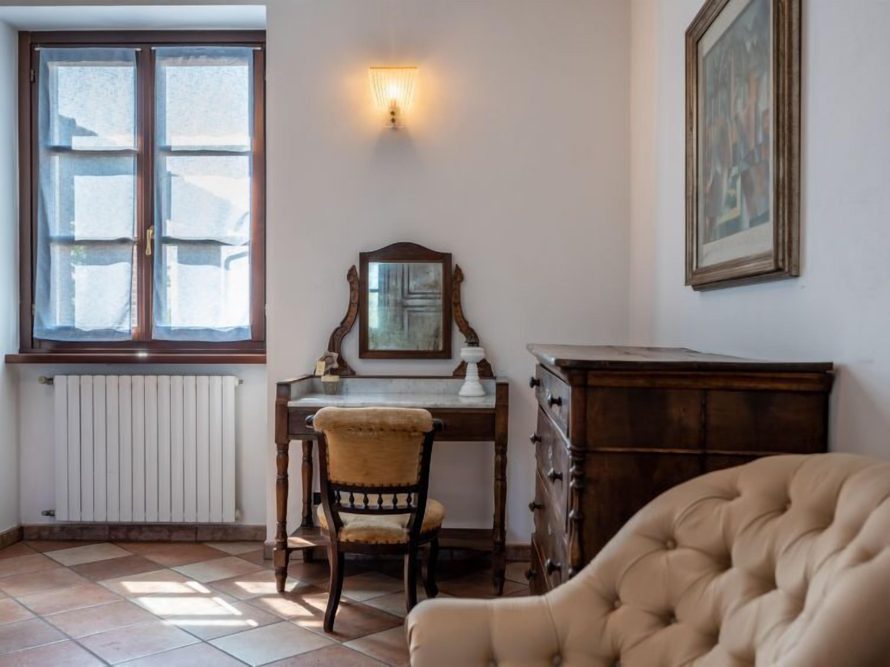 Een kamer met een houten bureau, een stoel, een radiator, een wandlamp en een lijst met een afbeelding.