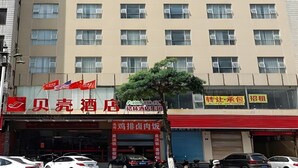 A hotel with multiple floors, featuring a red and beige facade, several flags, and a tree in front. - Shell Putian Hanjiang District Hanhua West Road Hotel (Putian)