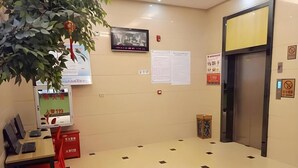A hotel lobby with a tiled floor, a desk with a computer, a chair, a television, and a red lantern hanging from a plant. - Shell Putian Hanjiang District Hanhua West Road Hotel (Putian)