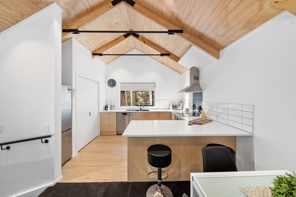 Une cuisine moderne avec des meubles blancs, un îlot central et un plafond en bois.