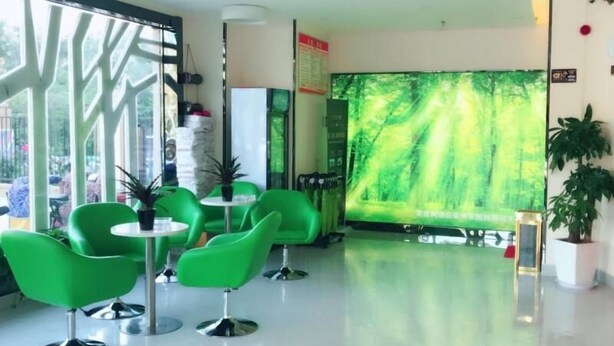 A modern interior with green chairs and tables, a large window with a tree pattern, and a wall with a green forest mural. - Vatica Hotel Bozhou Qiaocheng District Guogou Guanlantianxia (Bozhou)