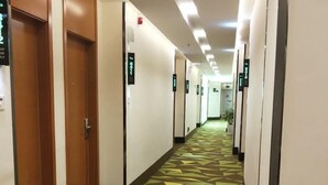 A hotel hallway with a geometric patterned floor, doors on the left, and directional signs on the walls. - Vatica Hotel Bozhou Qiaocheng District Guogou Guanlantianxia (Bozhou)