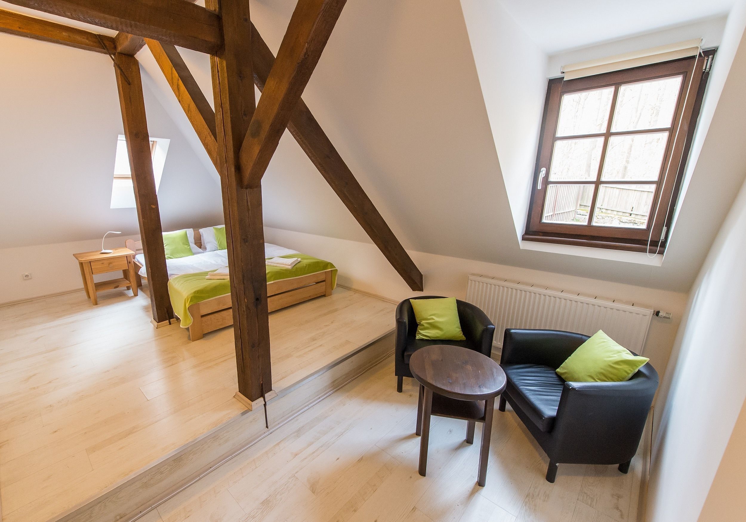 Quarto estilo loft com teto inclinado, cama, sofá, mesa pequena e janela com vista.