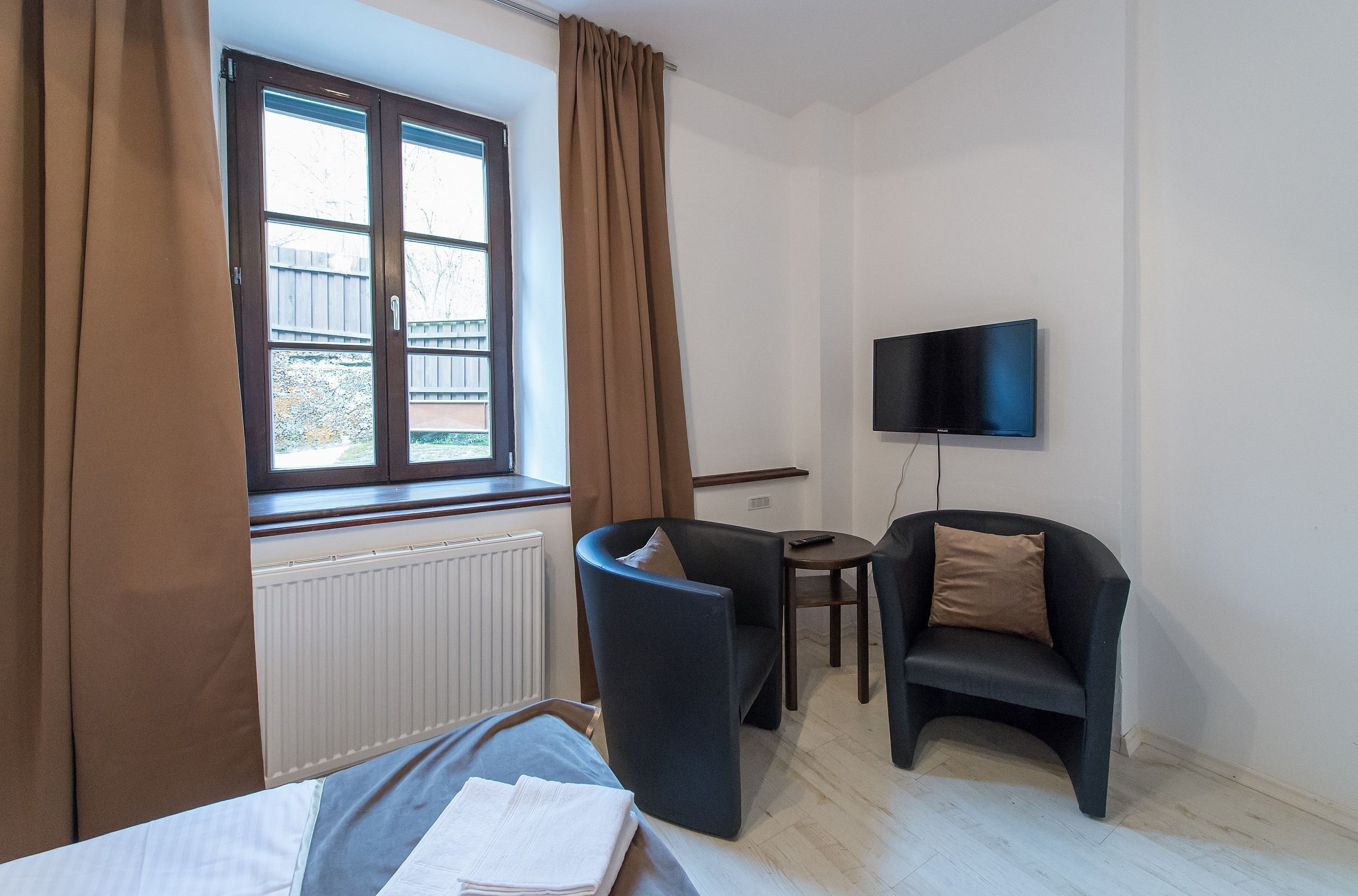A room with a bed, a chair, a small table, a TV, and a window with curtains.