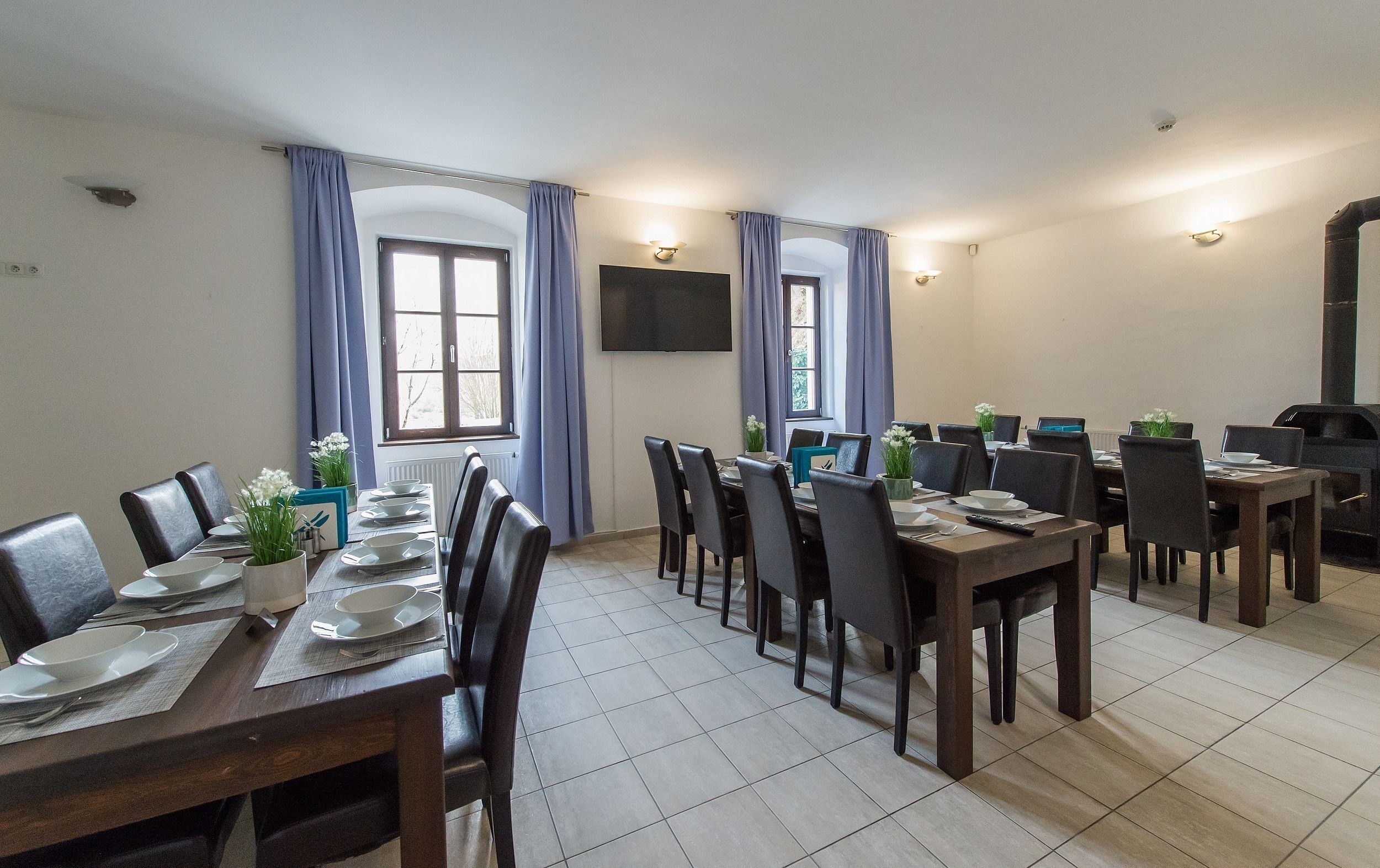 A dining area with multiple tables set for meals, a flat-screen TV mounted on the wall, and a fireplace.