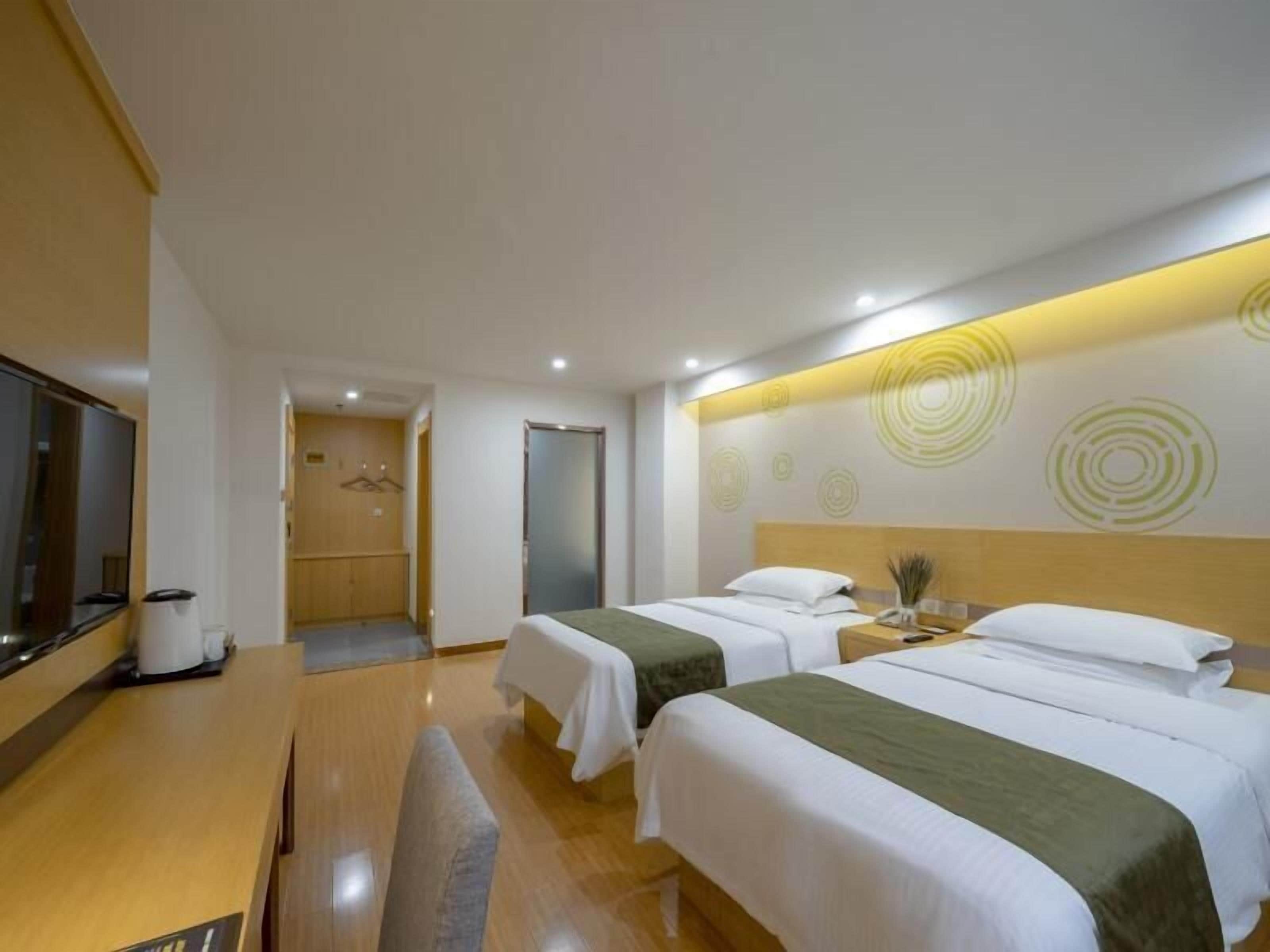 Habitación de hotel con dos camas, televisión, escritorio y baño visible a través de una puerta abierta.