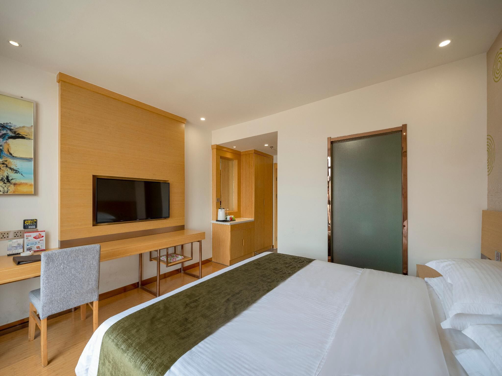 A hotel room with a bed, a desk with a chair, a television mounted on the wall, and a door.
