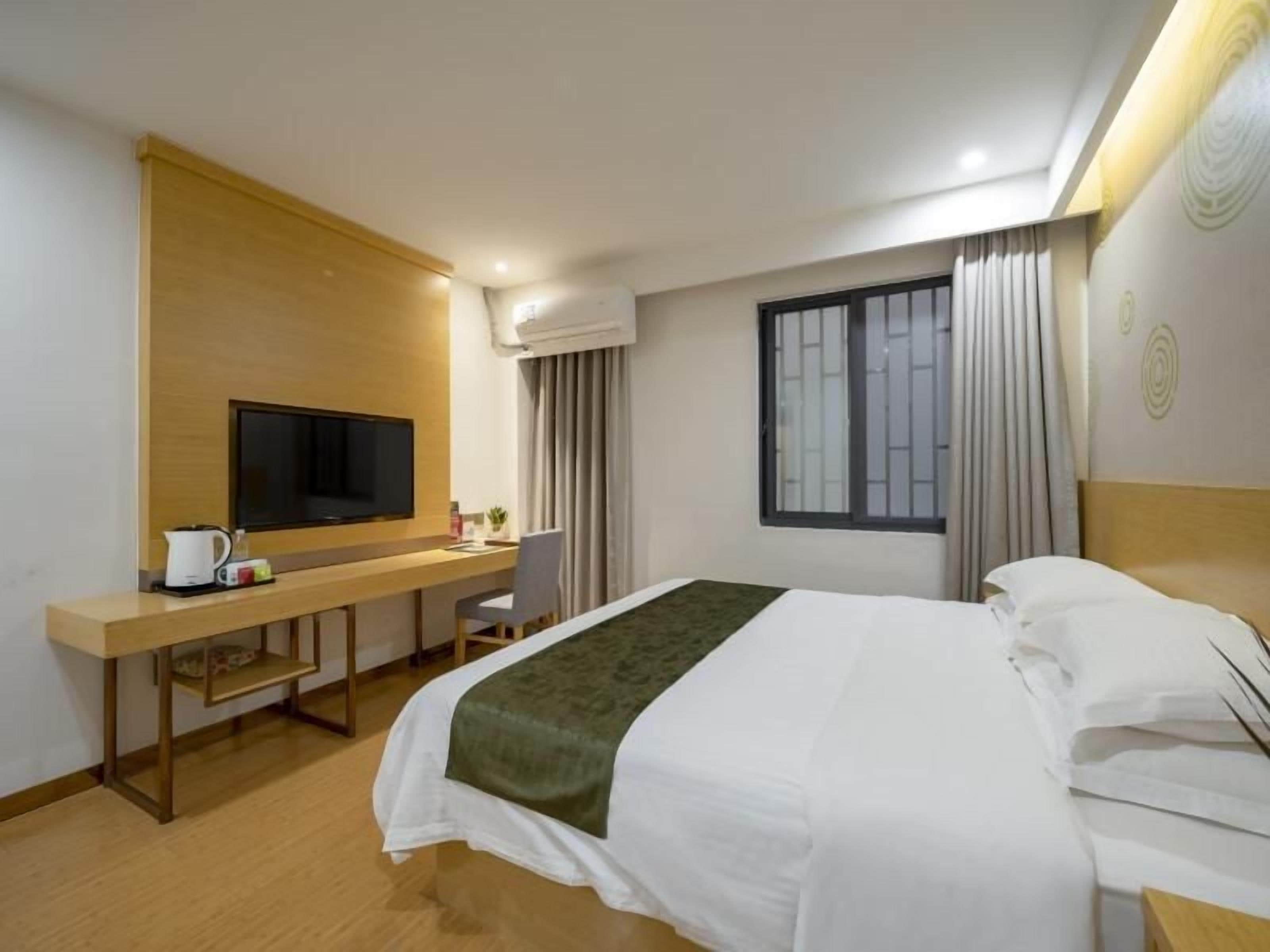 Ein Hotelzimmer mit einem Bett, einem Schreibtisch mit Fernseher, einem Sessel und einem fenster mit Vorhängen.